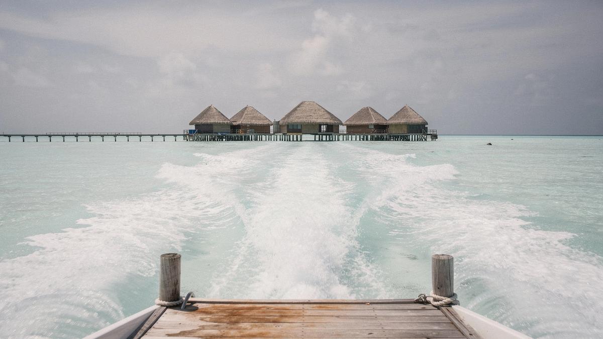 Speedboat wake crossing a pale lagoon toward a resort jetty in the Maldives